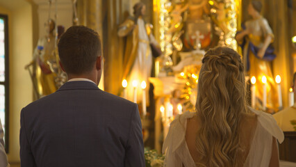 CLOSE UP: Back view of young newlyweds standing during wedding mass in church