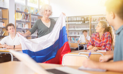 Pupils having lesson of geography. Female teacher discussing with children about national flag of...