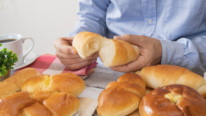 白い木目テーブルの上のパンとコーヒー｜パンを食べる男性