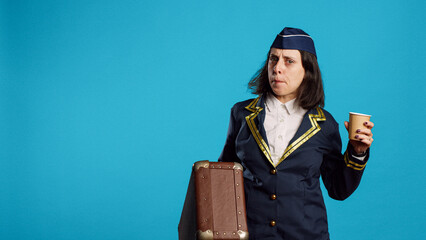 Smiling air hostess carrying suitcase to leave for work, drinking coffee and getting ready for departure. Stewardess preparing to fly on airplane, holding briefcase and feeling confident.