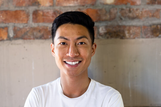 Portrait of happy asian casual businessman smiling against brick wall in office