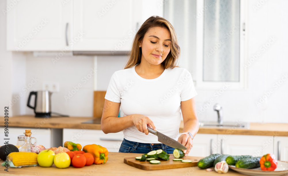 Wall mural young smiling woman chopping vegetables in home kitchen, preparing vegan dish