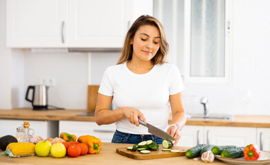 Obraz na płótnie Canvas Young smiling woman chopping vegetables in home kitchen, preparing vegan dish