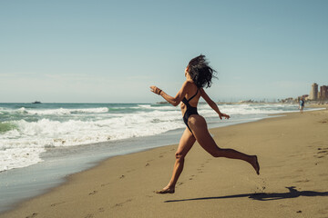 a beautiful girl in a black swimsuit with a smile runs into the sea on a summer day