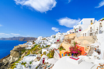 The picturesque whitewashed village of Oia Greece, with the Blue Dome Church in view among the hotels and resorts on the island of Santorini. - obrazy, fototapety, plakaty