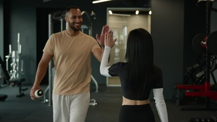 Back view sportswoman tired fit woman walk in fitness gym wipe towel after sport workout meet african american man trainer give high five to sportsman diverse athletes bodybuilders colleagues greeting - Powered by Adobe