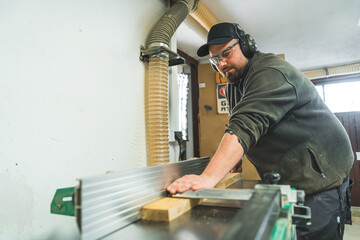 A woodworking machine used to produce a flat surface along a board's length. Focused woodworker in protective gear working. High quality photo