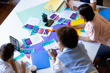 High angle of busy diverse designers using tablet and discussing visuals at design meeting