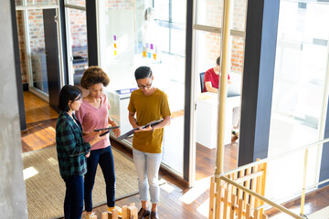 High angle of diverse creative colleagues using tablet and discussing in office corridor, copy space