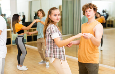 Pairs of teengers standing in dance studio and holding each other hands during their repetition.