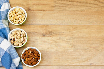 nuts (almonds, pistachio, cashews) in bowls on wooden table