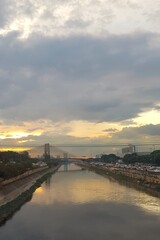 sunset in front of a river in the middle of the city, on top of a bridge full of traffic