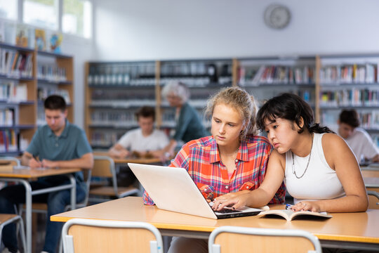 Portrait of asian schoolgirl with her spanish female friend studying in library using laptop