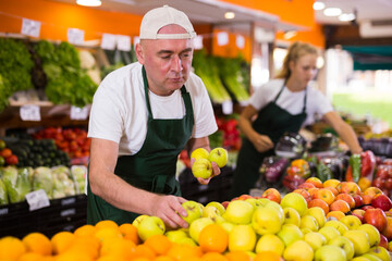 Man seller working in a supermarket in the vegetable department puts fresh apples on the counter for sale