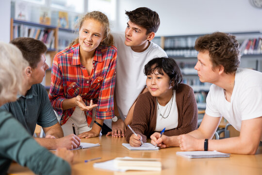 Positive teenage students working and discussing in groups in college library