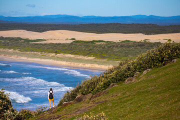 Fototapeta na wymiar beautiful backpacker girl enjoying spectacular view of new south wales coast in hat head national park, australia; sand dunes and long beach on the shore of pacific during sunrise