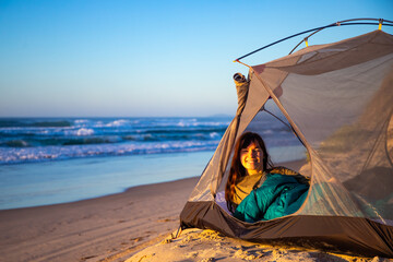 Fototapeta na wymiar A beautiful girl admires a wonderful sunrise on the beach from her tent. Camping on the beach in Australia, Hat Head National Park, NSW