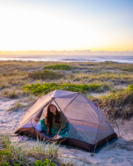 pretty girl camping in the tent on the sand dunes in new south wales, australia, sleeping in the tent on australian beach in front of pacific ocean, transparent tent on the beach