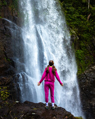 close up on a beautiful, brave, long haired girl standing in front of a large waterfall in...