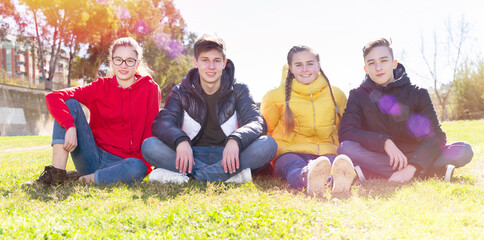 Fototapeta premium Group of teenagers chatting while sitting on green spring lawn