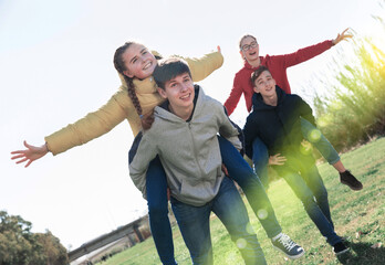 Group of laughing teenagers spending time together on spring day, girls riding piggy-back on boys. Concept of happy adolescence