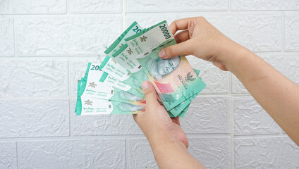 Rupiah banknotes in female hand on white wall