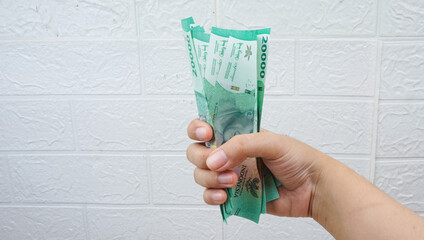 Female hand squeezing tightly some banknotes, on white wall