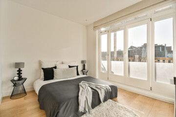 a bedroom with white walls and hardwood flooring in the middle of the room, there is a large window that looks out onto the city