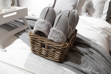 Fototapeta na wymiar Leather gray with white fur house slippers in a wicker basket on the bed in the hotel