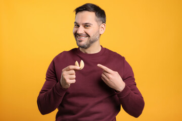 Happy man holding tasty fortune cookie with prediction on orange background