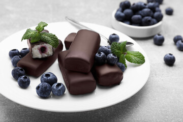Delicious glazed curd snacks with fresh blueberries and mint on light grey table, closeup