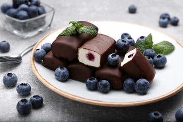 Delicious glazed curd snacks with fresh blueberries and mint on light grey table
