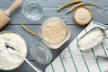 Leaven, flour, water, whisk and ears of wheat on grey wooden table, flat lay