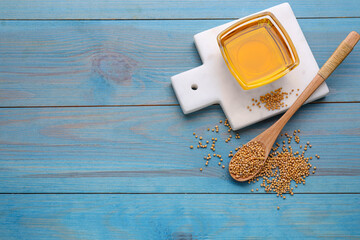 Bowl of natural oil and mustard seeds on light blue wooden table, flat lay. Space for text