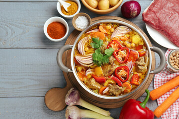 Delicious vegetable soup with meat in saucepan and ingredients on grey wooden table, flat lay. Space for text