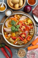 Delicious vegetable soup with meat in saucepan and ingredients on grey wooden table, flat lay