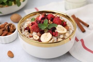 Delicious oatmeal with freeze dried berries, banana, nuts and mint on white table, closeup