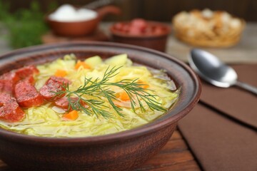 Bowl of delicious sauerkraut soup with smoked sausages and dill on table, closeup