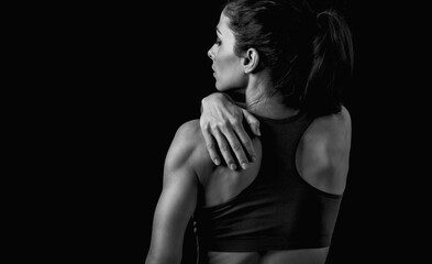 Female sporty muscular model with ponytail doing correction massage holding the hand the low back on dark shadow black background with empty copy space. Back view.