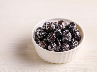 Black olives in white bowl on white background. Dried ripe fruits of Olea europaea, one of the core ingredients in Mediterranean cuisine. Edible, raw, organic food. Close up macro photo.