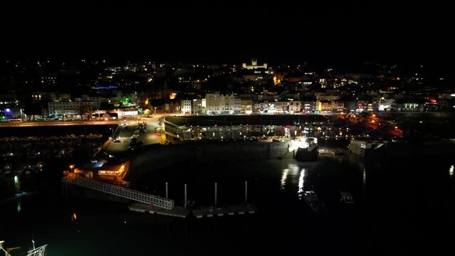 Night flight into St Peter Port Harbour Guernsey featuring visitors marina and sea front with buildings lit in the background including Elizabeth College