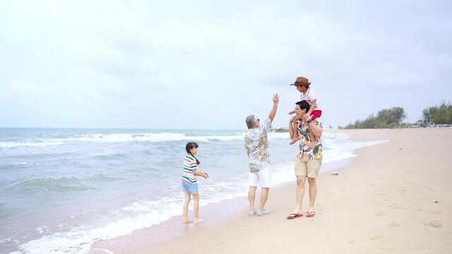 Group of Asian Multi-Generation family in casual clothing enjoy and fun outdoor lifestyle walking and playing together at tropical beach during travel island ocean at sunset on summer holiday vacation