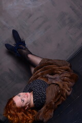 red-haired woman in a black dress with polka dots and in mink coat lies on the Black floor with her feet up raise her legs in blue boots sexy middle age