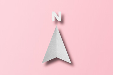 White paper cut in north arrow shape set on pink paper background.