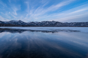 Fototapeta na wymiar 雲の流れる青空を湖面に反射する冬の湖。北海道の屈斜路湖。