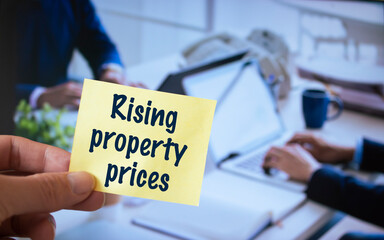 Male hand holding sticky note written Rising property prices.