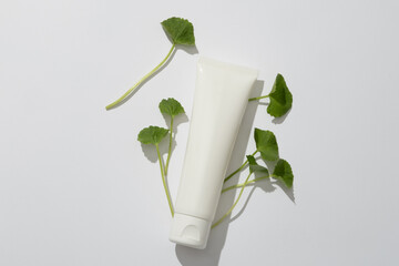 Minimal scene for design with copy space - an unbranded plastic tube and fresh gotu kola leaves on...