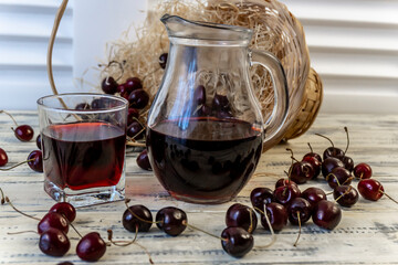 Cherry and cherry juice or wine on a wooden table, a decanter and a glass with juice, a basket with...