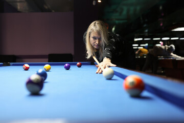 Focused woman hits white ball leaning above blue pool table