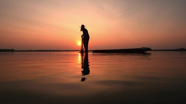 Silhouette fisherman throwing net casting fish in early morning with wooden boat with a flock of birds, Fisherman life style